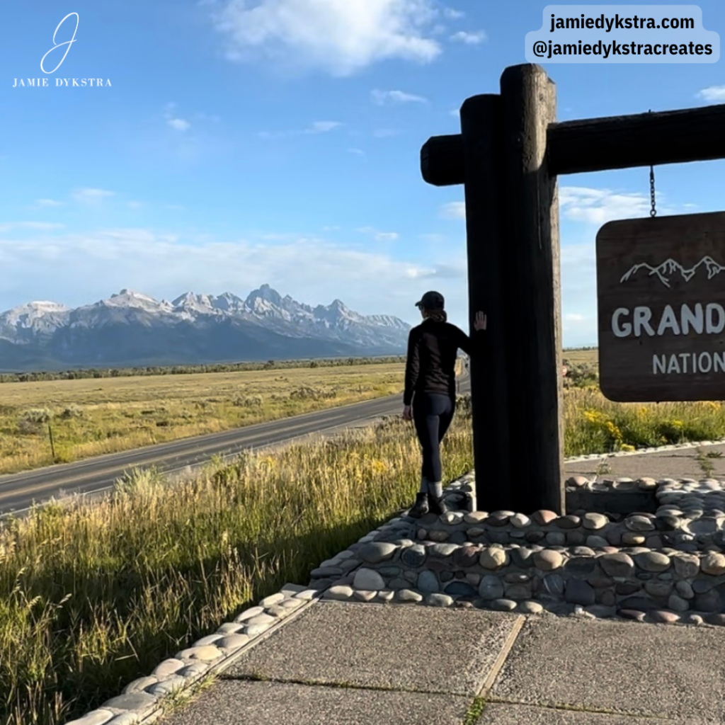 A picture of me facing the Grand Tetons leaning on the Grand Teton National Park sign.