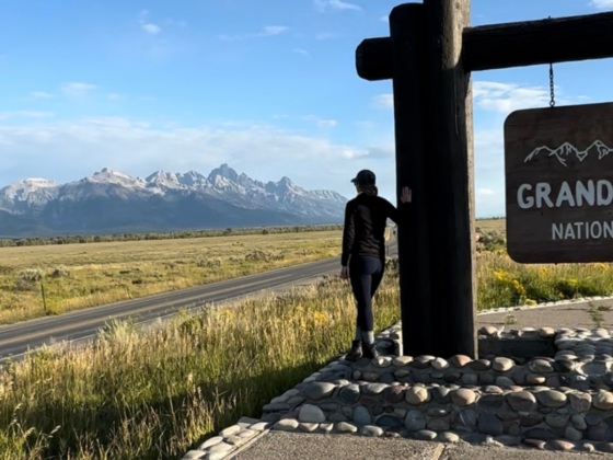 A picture of me facing the Grand Tetons leaning on the Grand Teton National Park sign.