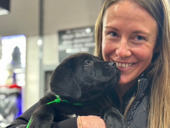 A picture of me holding a black lab puppy with him looking at me.