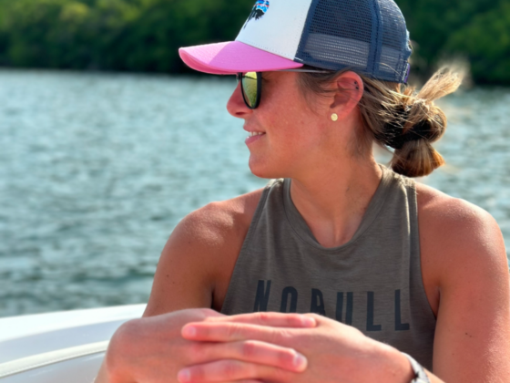 A picture of me in a pink and navy baseball hat with a dark green tank top on a boat.