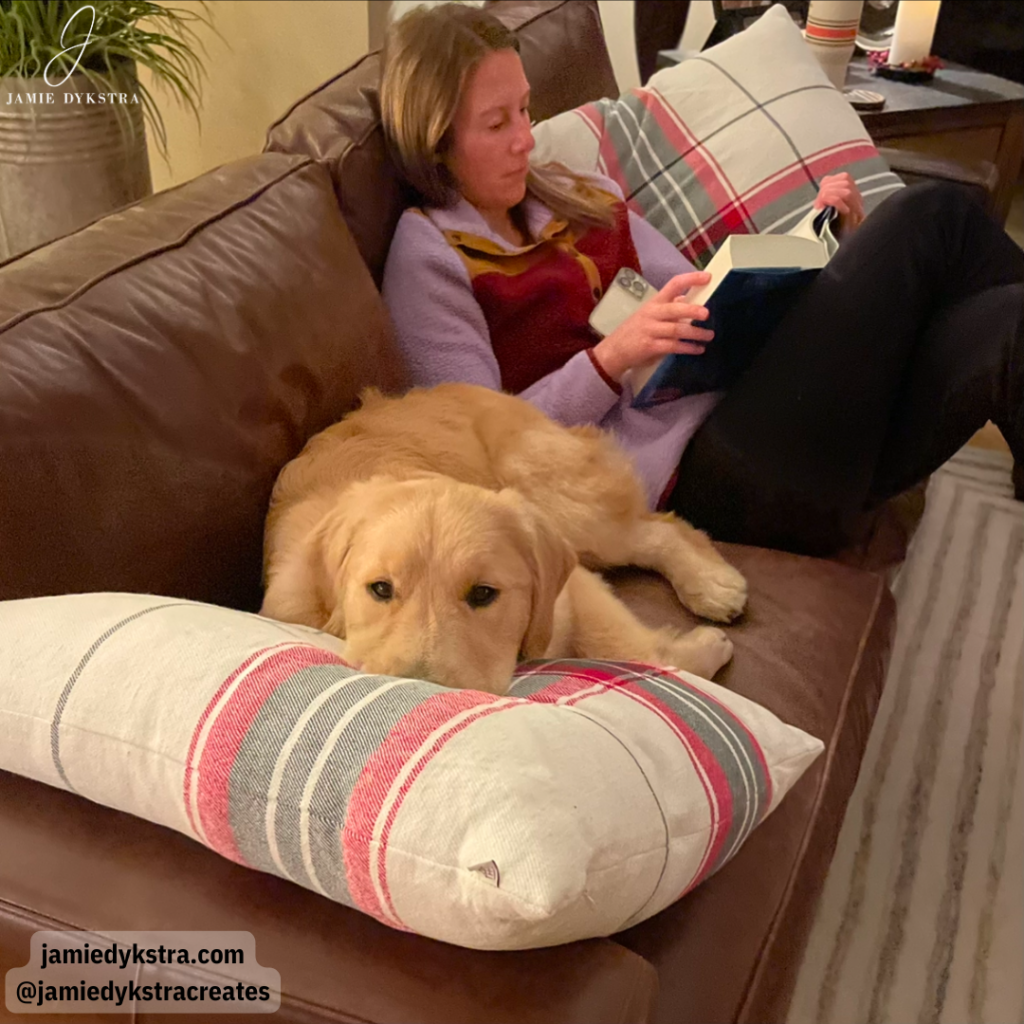 A picture of me reading on the couch with my Golden retriever laying next to me with his head on a pillow.
