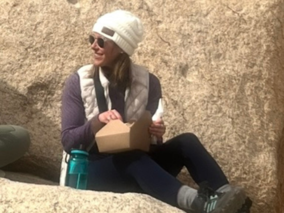I picture of me sitting on a large rock at Joshua Tree National Park eating a packed lunch.