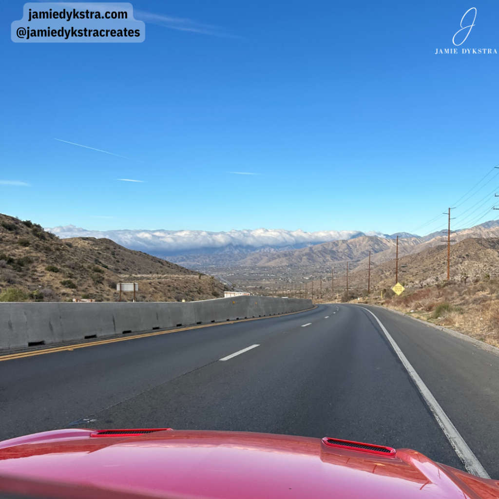 A picture on a highway coming down a mountain highway to a plume of clouds.