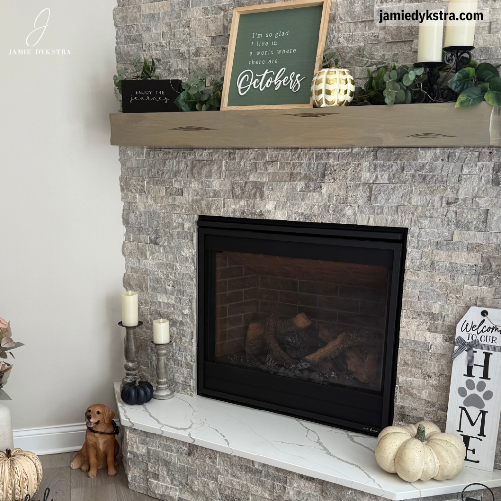 A picture of a fireplace with gray stone surrounded by fall decorations.