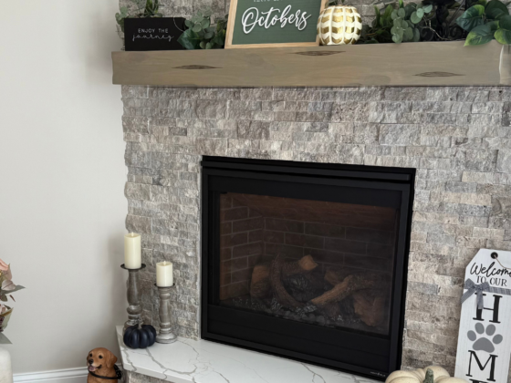 A picture of a fireplace with gray stone surrounded by fall decorations.