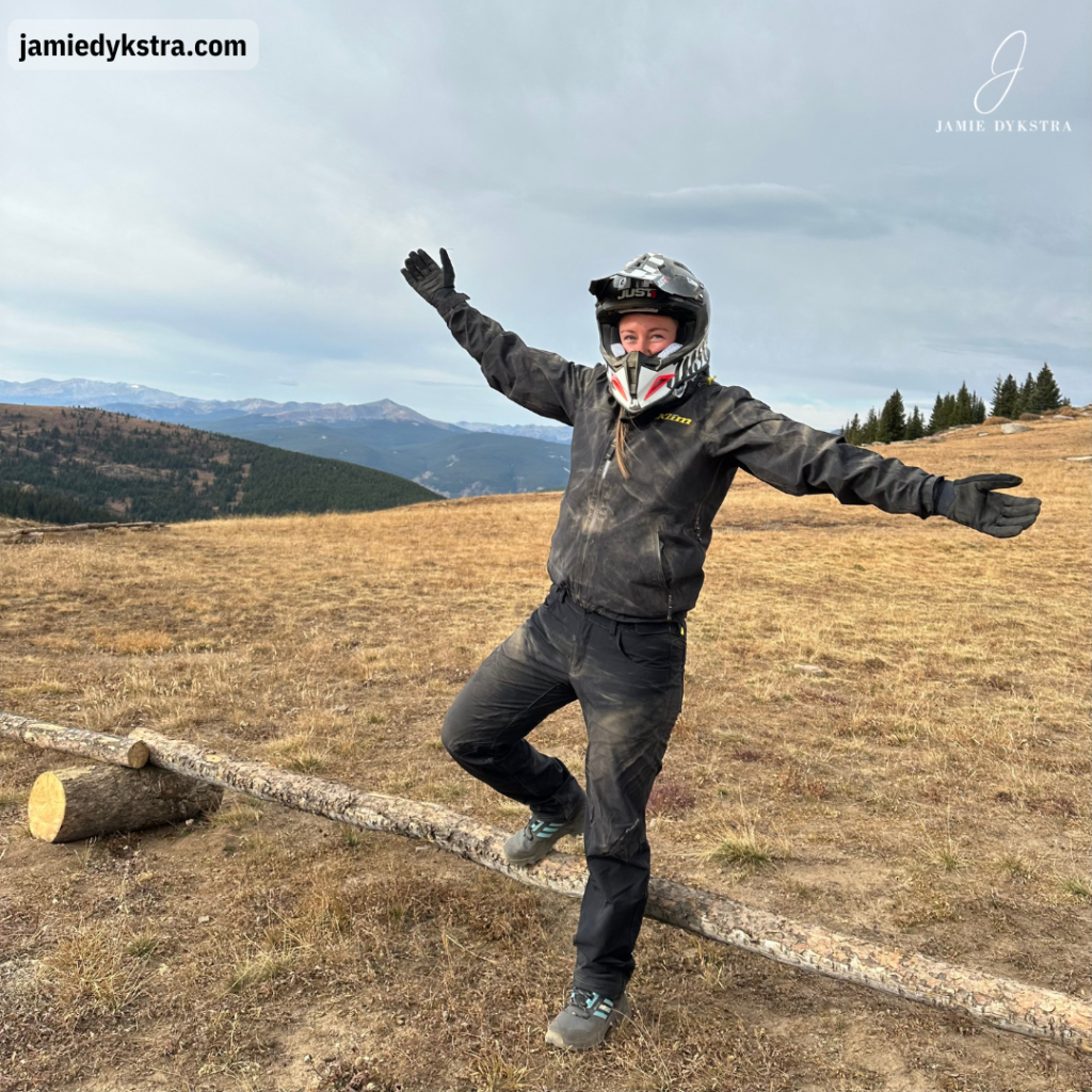 A picture of me in a helmet and dusty riding gear with arms spread out at the top of a mountain after riding side by sides up the trail.