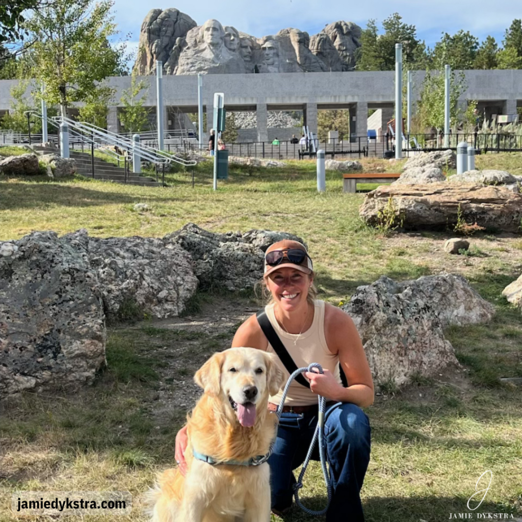 A picture of me kneeling next to a Golden Retriever outside of Mount Rushmore.