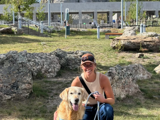 A picture of me kneeling next to a Golden Retriever outside of Mount Rushmore.