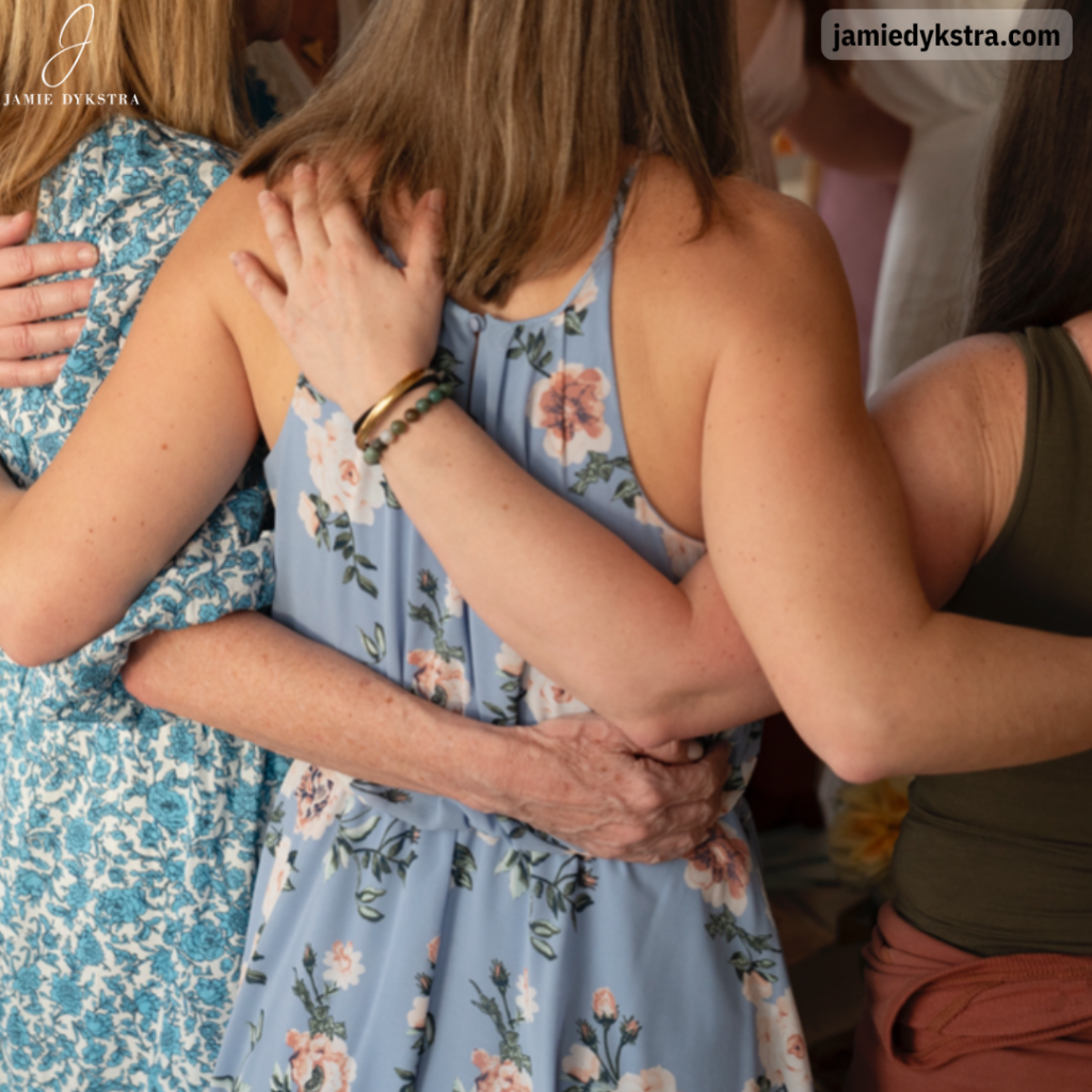 A photo of the back of me in a blue flowery dress with my arms around two other women.