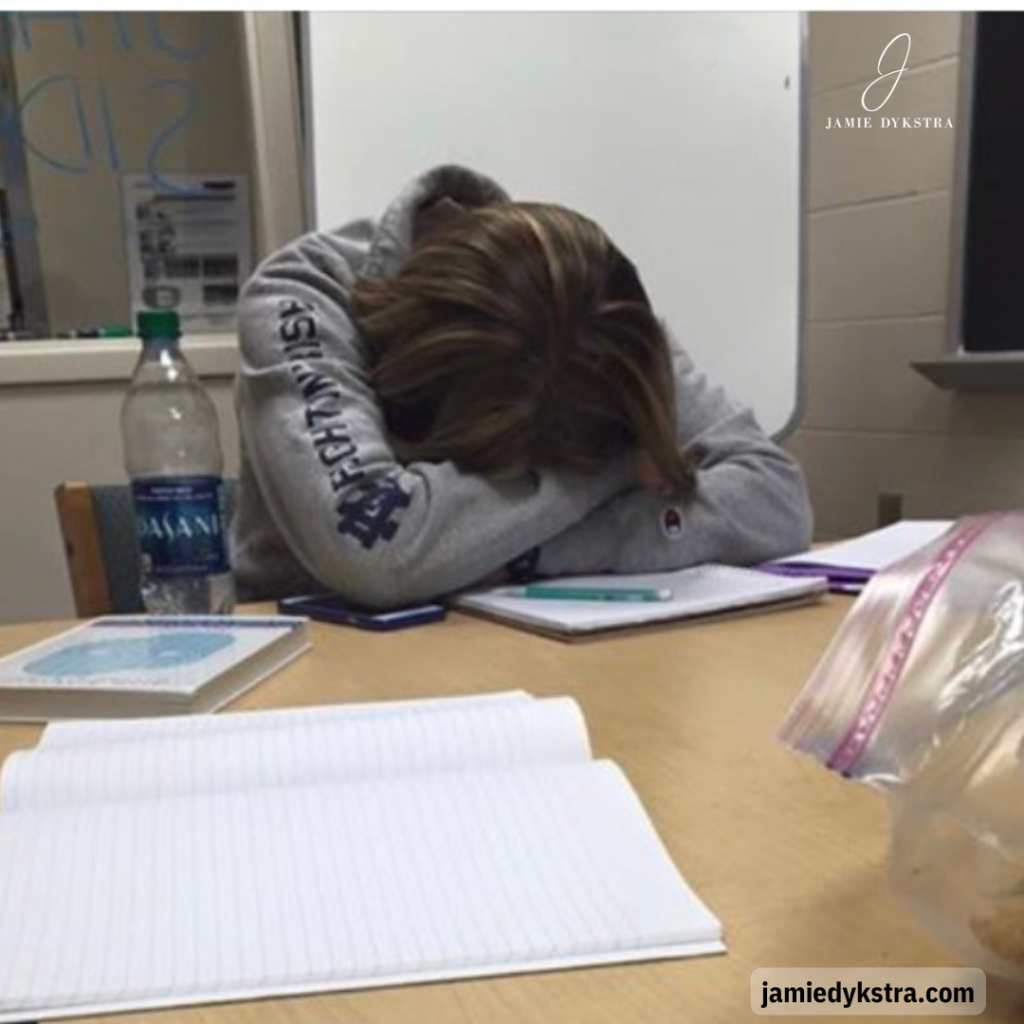 A photo of me with my head down in my arms on a table with books and notebooks in front of me.