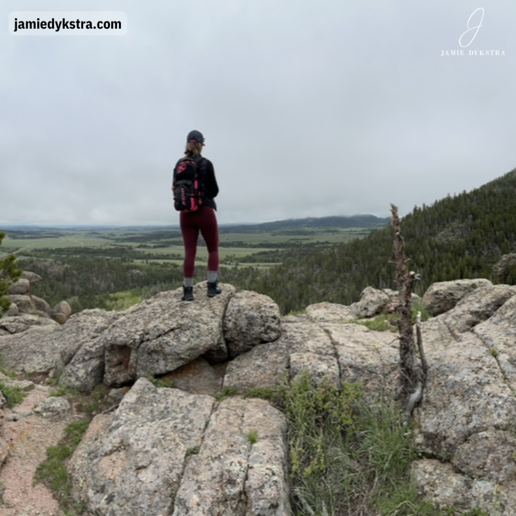 A photo of me standing on some large rocks on a mountain with my back to the camera overlooking a valley and foothills.