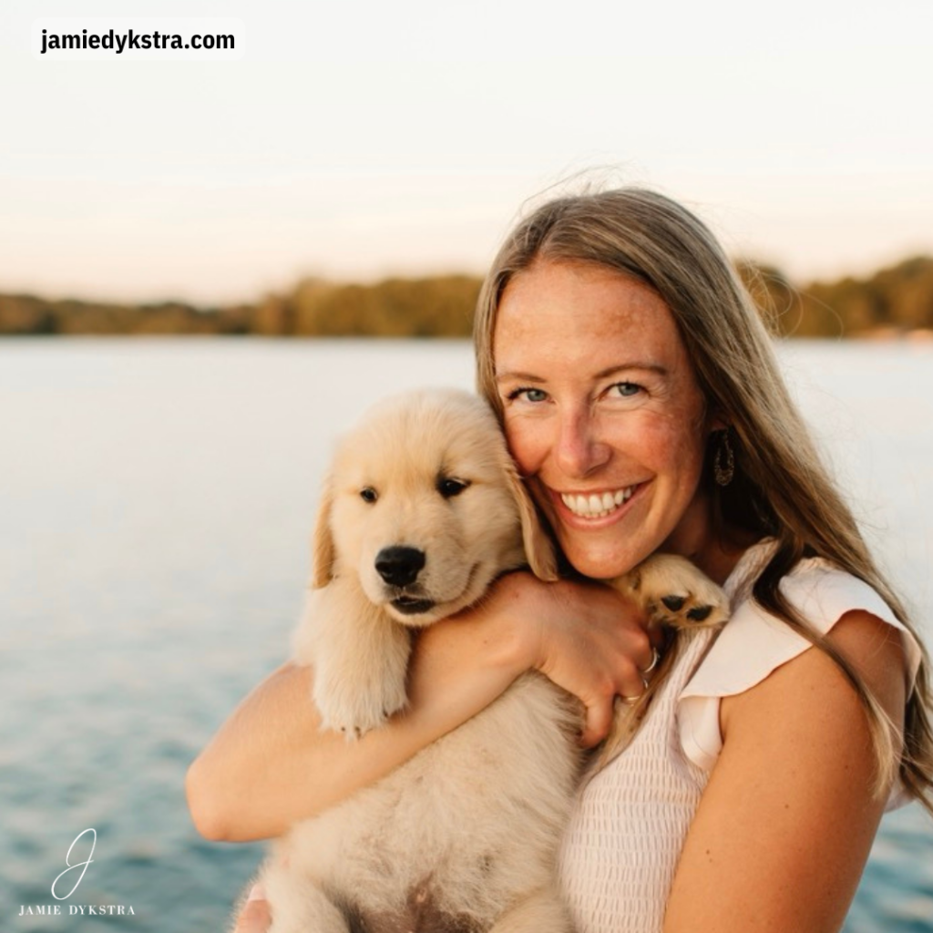 A photo of me in a cream dress standing on a pier holding a Golden Retriever puppy at sunset.