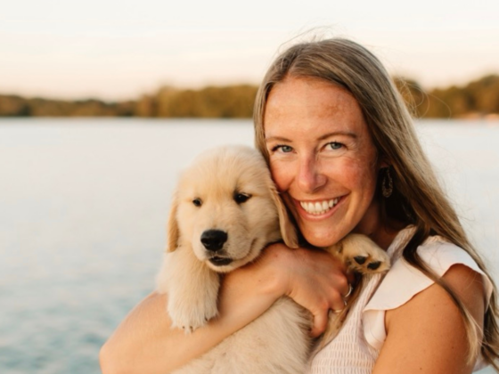 A photo of me in a cream dress standing on a pier holding a Golden Retriever puppy at sunset.