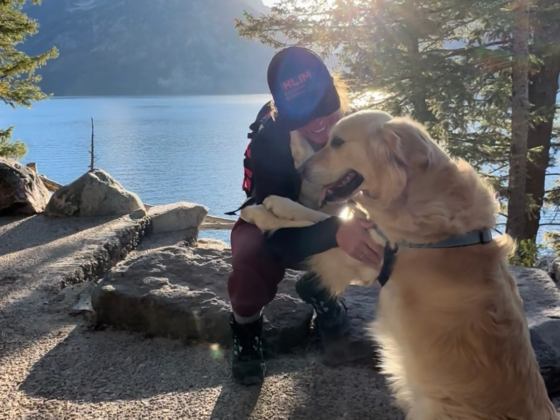 A photo of me hugging a golden retriever in front of a lake and a mountain.