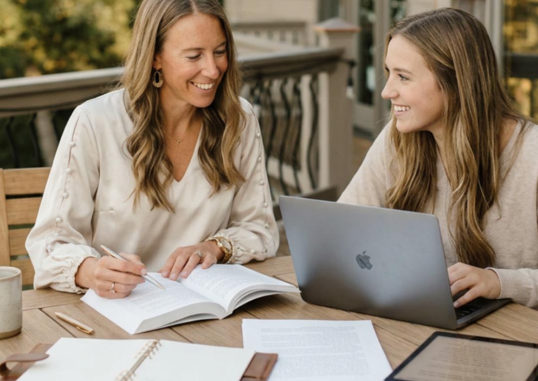 two women writing together on a deck outside
