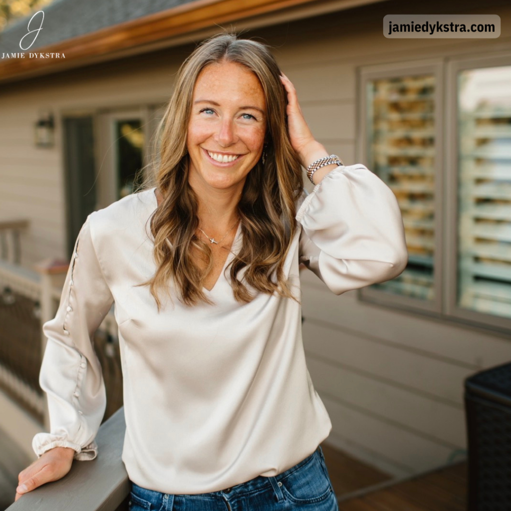 A photo of me standing on a deck with a cream silk shirt, jeans, and my hand in my hair.