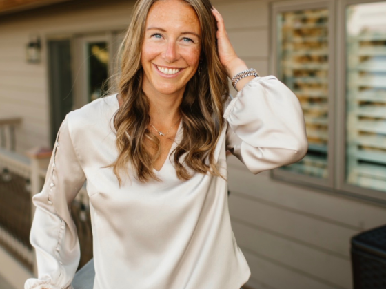 A photo of me standing on a deck with a cream silk shirt, jeans, and my hand in my hair.