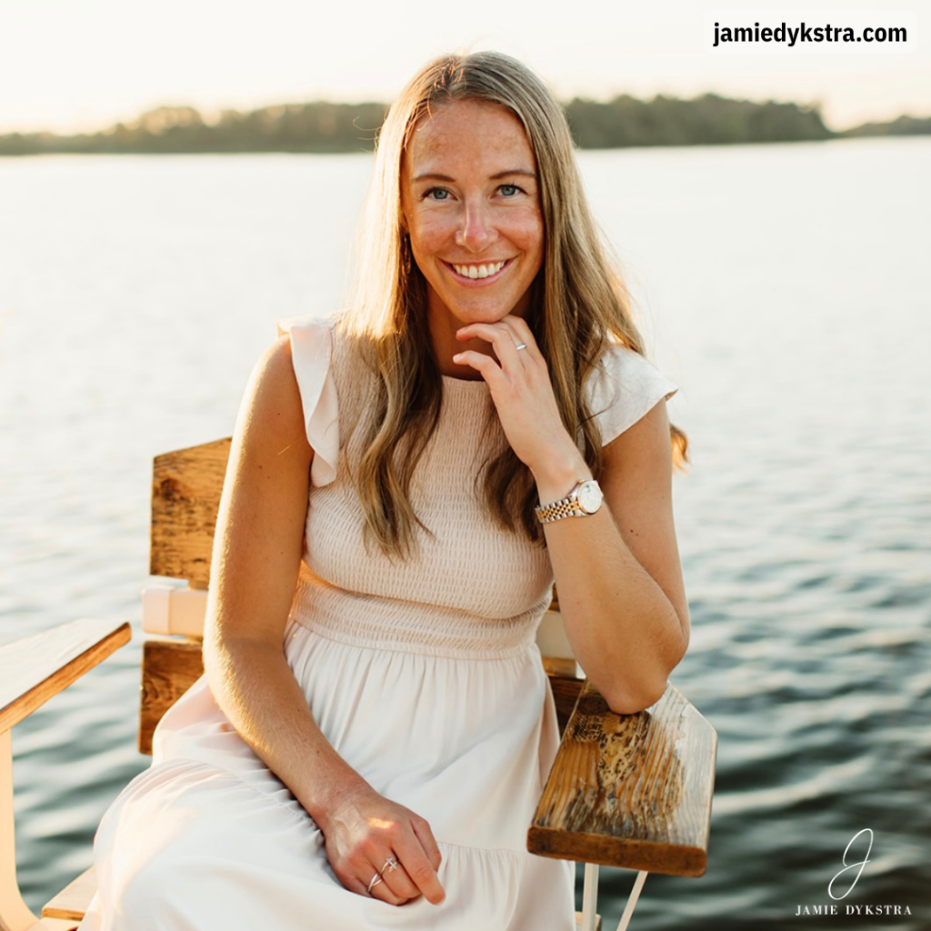 A photo of me sitting on a chair in a cream dress with a lake in the background at sunset.
