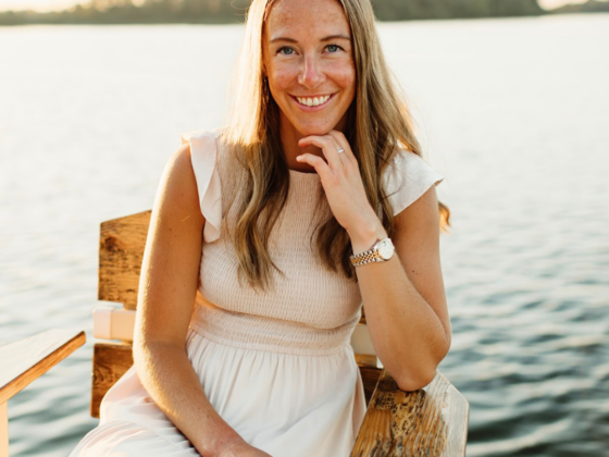 A photo of me sitting on a chair in a cream dress with a lake in the background at sunset.